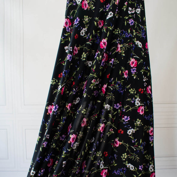 Create a look you’ll love in our timeless black DTY knit fabric with a floral print of pink, white, and purple flowers and soft green leaves. A gorgeous knit with a soft hand and fluid drape, perfect for making a garment that flatters!  Image of fabric drape.
