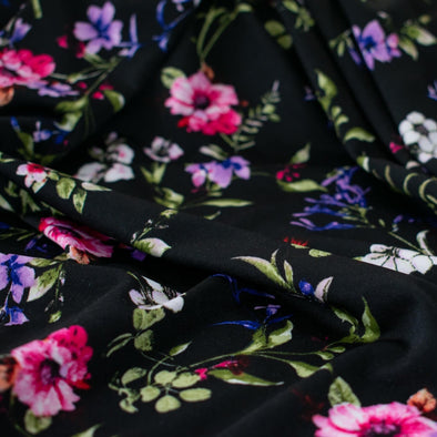 Create a look you’ll love in our timeless black DTY knit fabric with a floral print of pink, white, and purple flowers and soft green leaves. A gorgeous knit with a soft hand and fluid drape, perfect for making a garment that flatters!  Close up image.