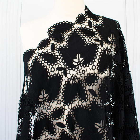 Sourced from a bridal and evening wear couture house comes this chic designer deadstock guipure lace fabric by the yard - a must have for any fashionista. The design showcases inky black maple leaves surrounded by eyelets and a double scalloped border, while the spaced thread bars (or brides) offer flexibility for incorporating the motif into your project. Image of fabric on dressform.