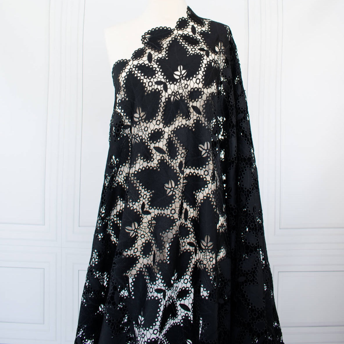 Sourced from a bridal and evening wear couture house comes this chic designer deadstock guipure lace fabric by the yard - a must have for any fashionista. The design showcases inky black maple leaves surrounded by eyelets and a double scalloped border, while the spaced thread bars (or brides) offer flexibility for incorporating the motif into your project. Image of fabric on dressform.