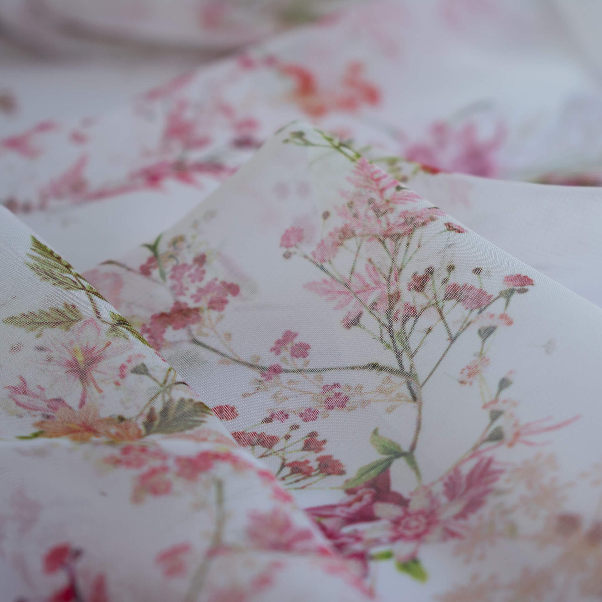 Close up image of Floral Couture designer soft white silk chiffon fabric with pink flowers and green leaves 