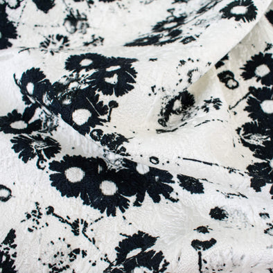 Close up image of couture black and white floral designer deadstock fabric by the yard! A modern floral design in black set against a creamy white is elevated by the soft "blistered" texture of this stunning jacquard. Perfect for wedding season.