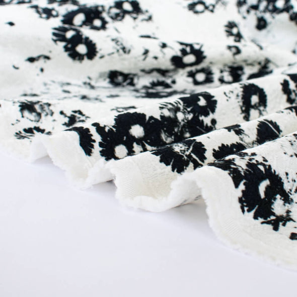 Close up image of couture black and white floral designer deadstock fabric by the yard! A modern floral design in black set against a creamy white is elevated by the soft "blistered" texture of this stunning jacquard. Perfect for wedding season.