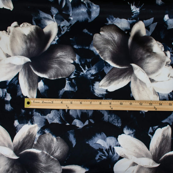Designer Deadstock Stretch Satin Floral print fabric by the yard. Create something special in this gorgeous stretch satin! Set against a black background the large floral print is in shades of pearl white, taupes, blues and grey. This would make a lovely fitted dress, pencil skirt, or separates. Image of fabric with ruler to show pattern scale.