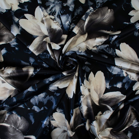 Designer Deadstock Stretch Satin Floral print fabric by the yard. Create something special in this gorgeous stretch satin! Set against a black background the large floral print is in shades of pearl white, taupes, blues and grey. This would make a lovely fitted dress, pencil skirt, or separates. Image of fabric twirled to demonstrate body.