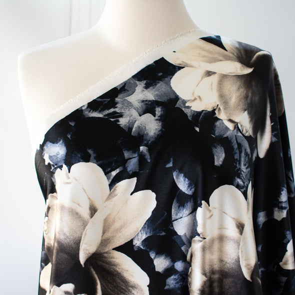 Designer Deadstock Stretch Satin Floral print fabric by the yard. Create something special in this gorgeous stretch satin! Set against a black background the large floral print is in shades of pearl white, taupes, blues and grey. This would make a lovely fitted dress, pencil skirt, or separates. Image of fabric on dressform.