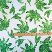 Designer Silk/Lycra Charmeuse Palm Print fabric by the yard! This fun and fashion forward deadstock fabric is perfect for creating unique and trending pieces. The green palm print set against a soft white background and the lustrous finish of this fabric will elevate any outfit.  Image of fabric scale with ruler.