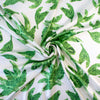 Designer Silk/Lycra Charmeuse Palm Print fabric by the yard! This fun and fashion forward deadstock fabric is perfect for creating unique and trending pieces. The green palm print set against a soft white background and the lustrous finish of this fabric will elevate any outfit.  Image of fabric body.