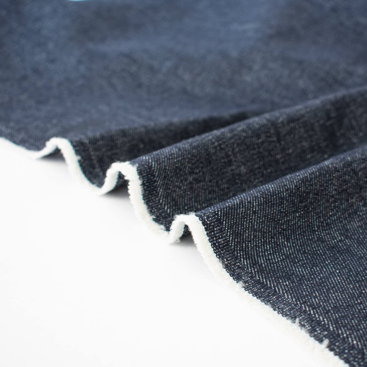 Create your own luxurious streetwear with this High End Designer deadstock denim fabric by the yard. 100% Cotton dark wash blue denim is robust with a textured stiff hand yet it still has some drape and a softness that feels good against the skin. Image of fabric selvedge.