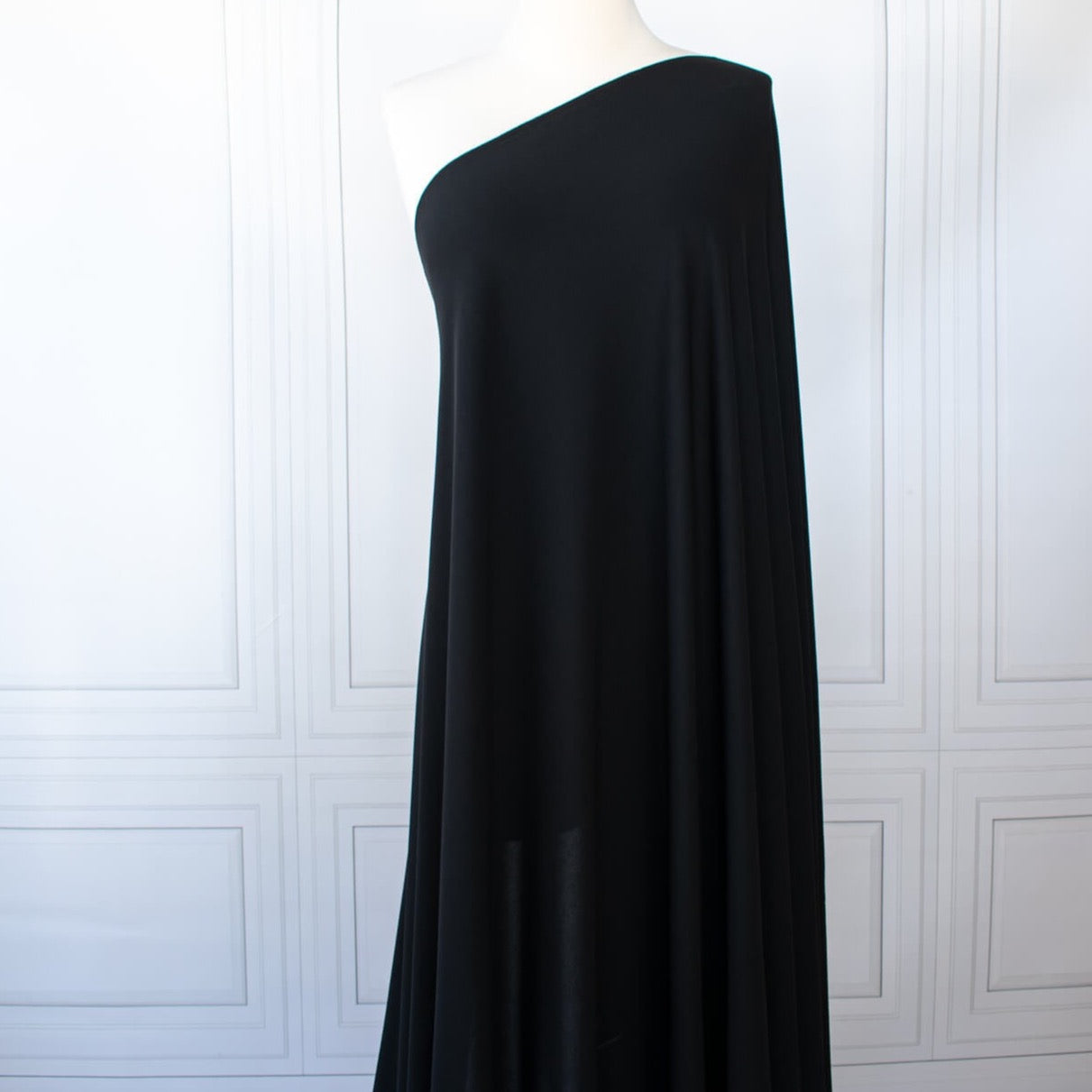 High-end Designer Black Matte jersey knit deadstock fabric by the yard, a timeless essential for every wardrobe. Achieve a designer-level look and feel, with a sophisticated black matte finish . Image of fabric on dressform.