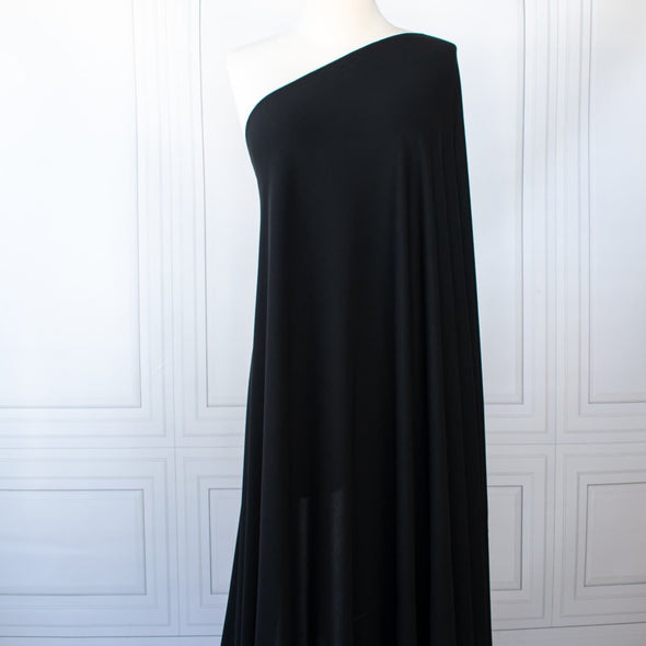 High-end Designer Black Matte jersey knit deadstock fabric by the yard, a timeless essential for every wardrobe. Achieve a designer-level look and feel, with a sophisticated black matte finish . Image of fabric on dressform.