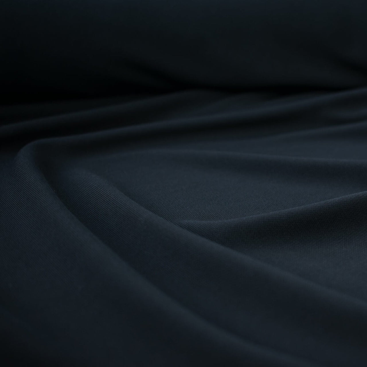 High-end Designer Black Matte jersey knit deadstock fabric by the yard, a timeless essential for every wardrobe. Achieve a designer-level look and feel, with a sophisticated black matte finish . Close up image.