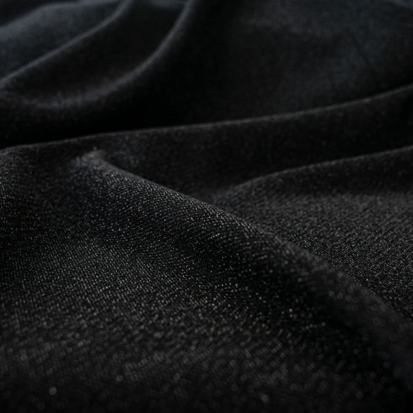 Feel glamorous with our Designer Shimmer Black Sweater Knit fabric by the yard - 'Fancy This'. This high-end designer deadstock knit in classic black with the perfect touch of sparkle. Soft and comfortable, this sweater is sure to become one of your favorite fashion staples. Close up image.