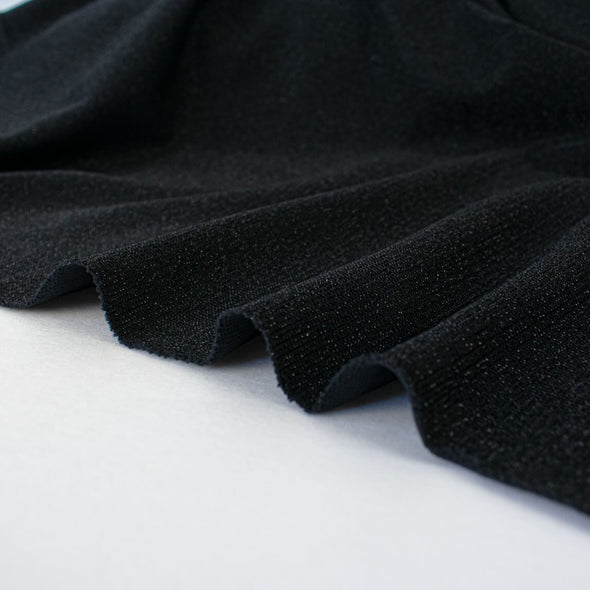 Feel glamorous with our Designer Shimmer Black Sweater Knit fabric by the yard - 'Fancy This'. This high-end designer deadstock knit in classic black with the perfect touch of sparkle. Soft and comfortable, this sweater is sure to become one of your favorite fashion staples. Image of fabric selvedge.