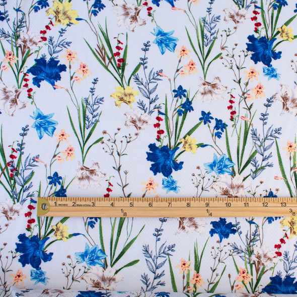 Italian crafted, soft white, viscose woven fabric by the yard. Gorgeous lilies and other florals in shades of peach, red, ivory and a vibrant blue with a fine jacquard pattern. Image of pattern scale with ruler.