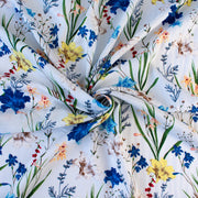 Italian crafted, soft white, viscose woven fabric by the yard. Gorgeous lilies and other florals in shades of peach, red, ivory and a vibrant blue with a fine jacquard pattern. Image of fabric body.