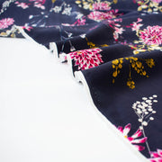 Italian Navy Floral Viscose Crepe fabric by the yard. This fabric features a beautiful design of vibrant blooms in shades of pink, and delicate sprays of flowers in soft white and ochre set against a navy background. The elegant drape and slightly textured crepe-like hand is perfect for your next high-end garment. Close up image of selvedge.