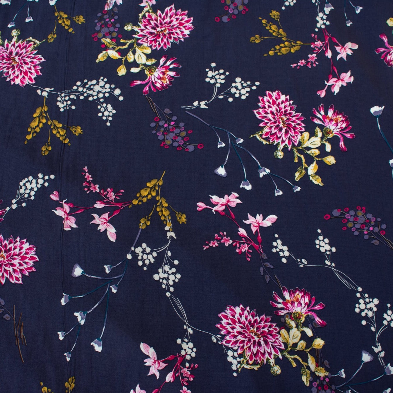 Italian Navy Floral Viscose Crepe fabric by the yard. This fabric features a beautiful design of vibrant blooms in shades of pink, and delicate sprays of flowers in soft white and ochre set against a navy background. The elegant drape and slightly textured crepe-like hand is perfect for your next high-end garment. Close up image.