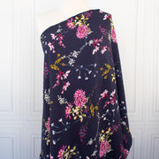 Italian Navy Floral Viscose Crepe fabric by the yard. This fabric features a beautiful design of vibrant blooms in shades of pink, and delicate sprays of flowers in soft white and ochre set against a navy background. The elegant drape and slightly textured crepe-like hand is perfect for your next high-end garment. Image of fabric draped on dressform.