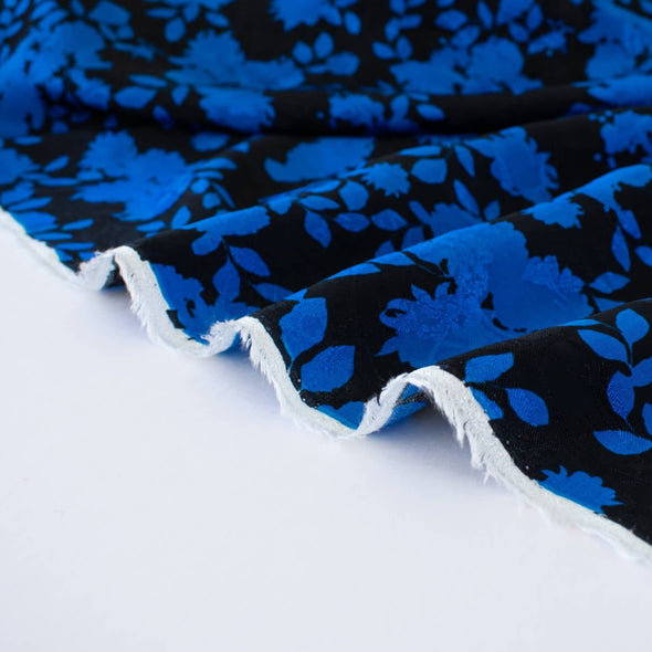 The 'Roses in Blue' Italian Jacquard fabric by the yard is just gorgeous! Luxurious and elegant, a beautiful black viscose fabric featuring a vibrant blue floral design that is sure to get you noticed.  Opaque with a nice drape and body, it is perfect for formal attire or a little something special.. Image of fabric selvedge.