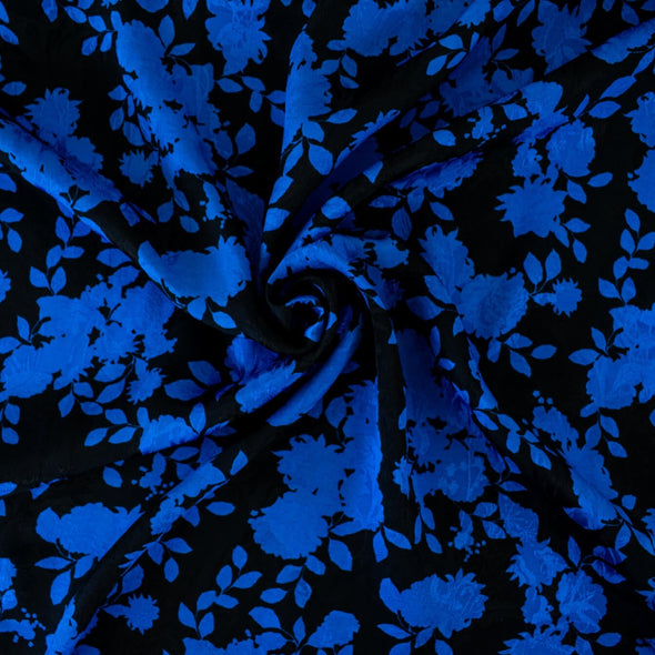The 'Roses in Blue' Italian Jacquard fabric by the yard is just gorgeous! Luxurious and elegant, a beautiful black viscose fabric featuring a vibrant blue floral design that is sure to get you noticed.  Opaque with a nice drape and body, it is perfect for formal attire or a little something special. Image of fabric swirled demonstrating body.