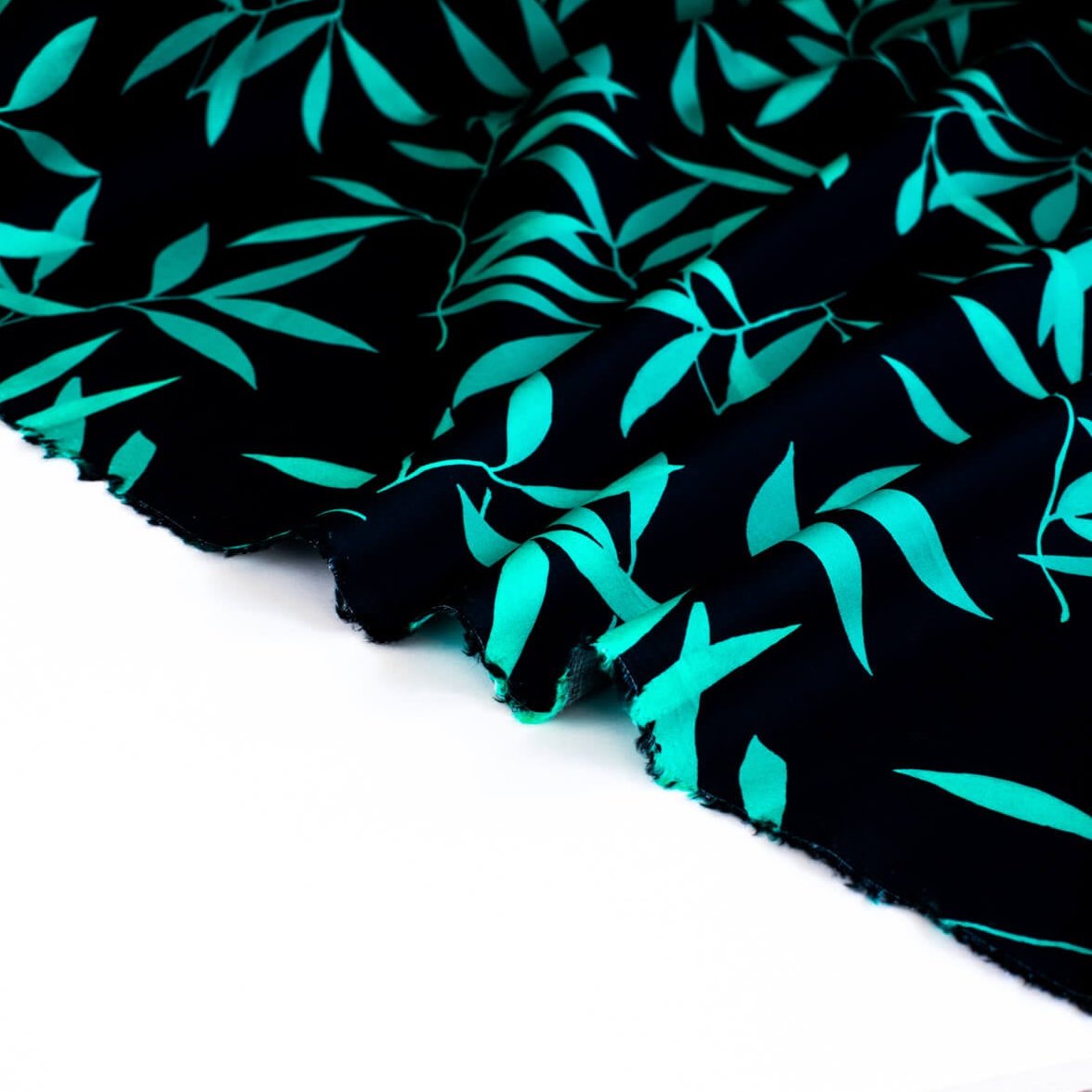 Carolina' cotton poplin designer fabric by the yard. This Italian poplin is light and billowy, perfect for sewing up tops, dresses and skirts. Made with stretch for ultimate comfort, this fabric is perfect if you want to add a touch of the exotic with its turquoise bamboo leaf print set against a black background. Image of fabric selvedge.