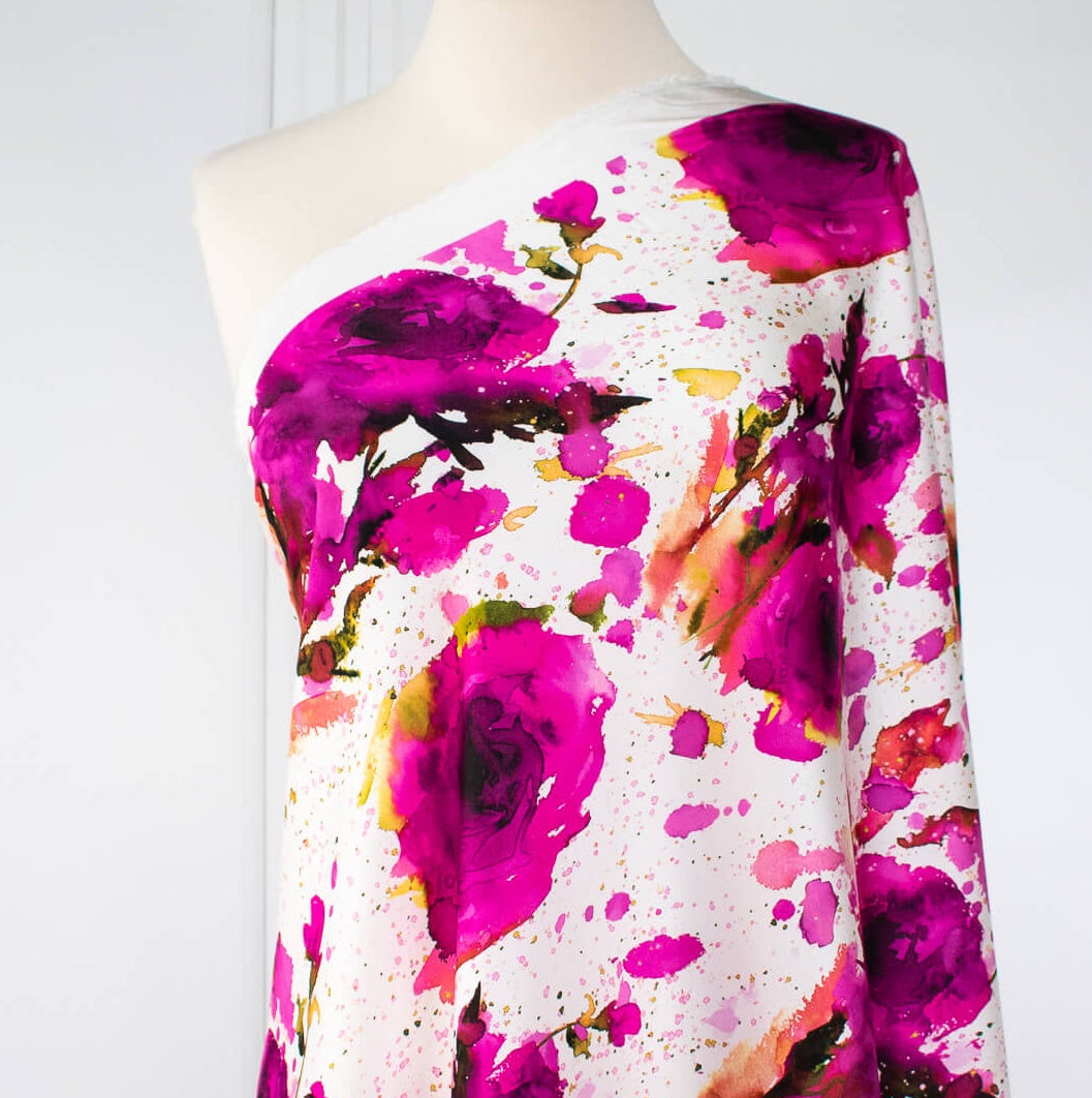Image of designer Italian satin viscose woven fabric on dress form. Featuring an exquisite watercolor floral pattern of dark pink abstract roses against a soft white background.