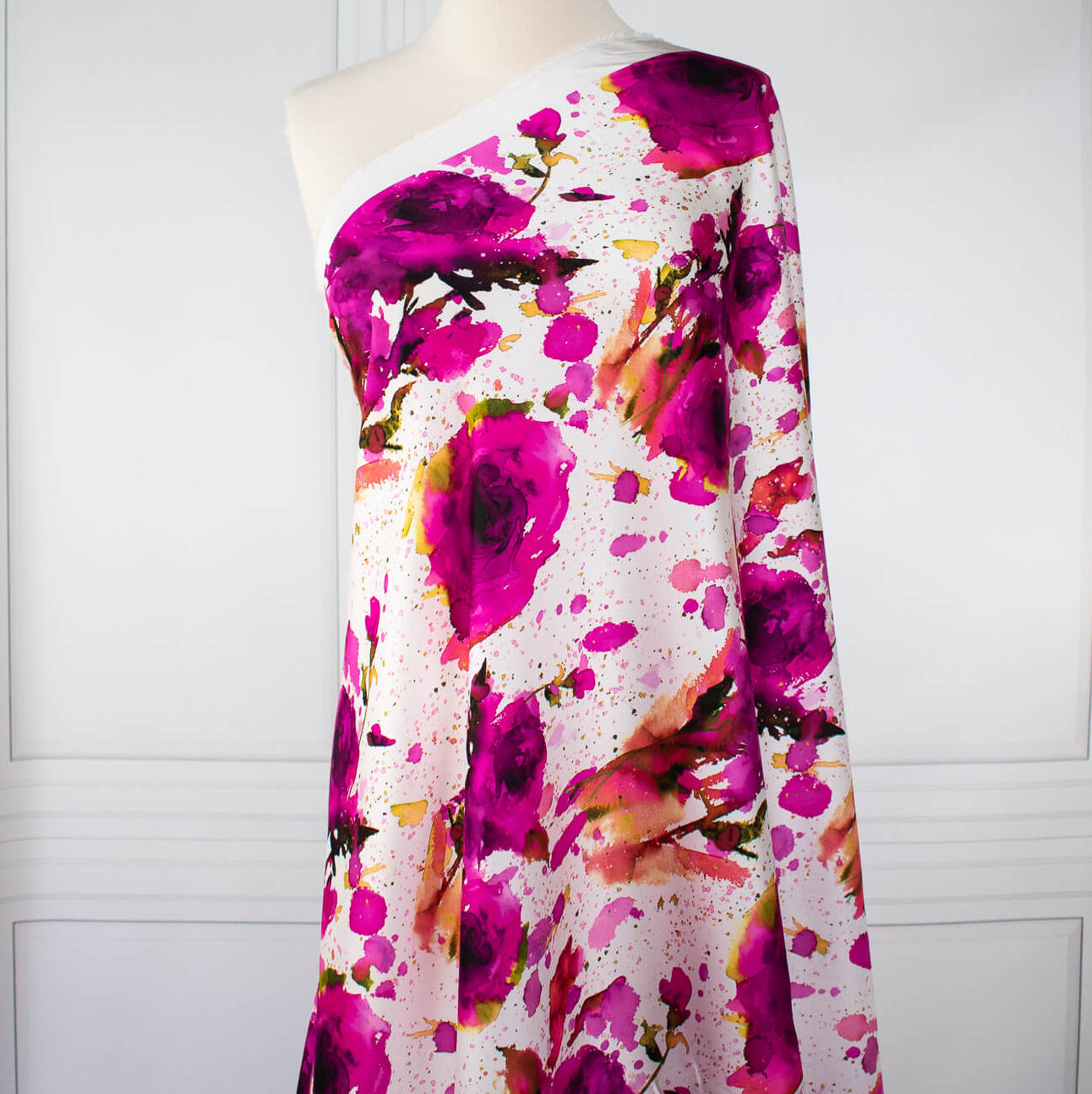 Image of designer Italian satin viscose woven fabric on dress form. Featuring an exquisite watercolor floral pattern of dark pink abstract roses against a soft white background.