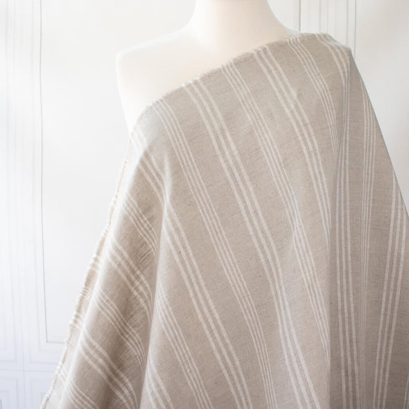 Experience the luxury of European linen fabric in a classic horizontal stripe. This medium weight linen would make a stunning jacket, skirt or pant. Featuring a wide width, textured hand, and sets of wide and narrow off white stripes. Photo of fabric draped on dress form to demonstrate scale.