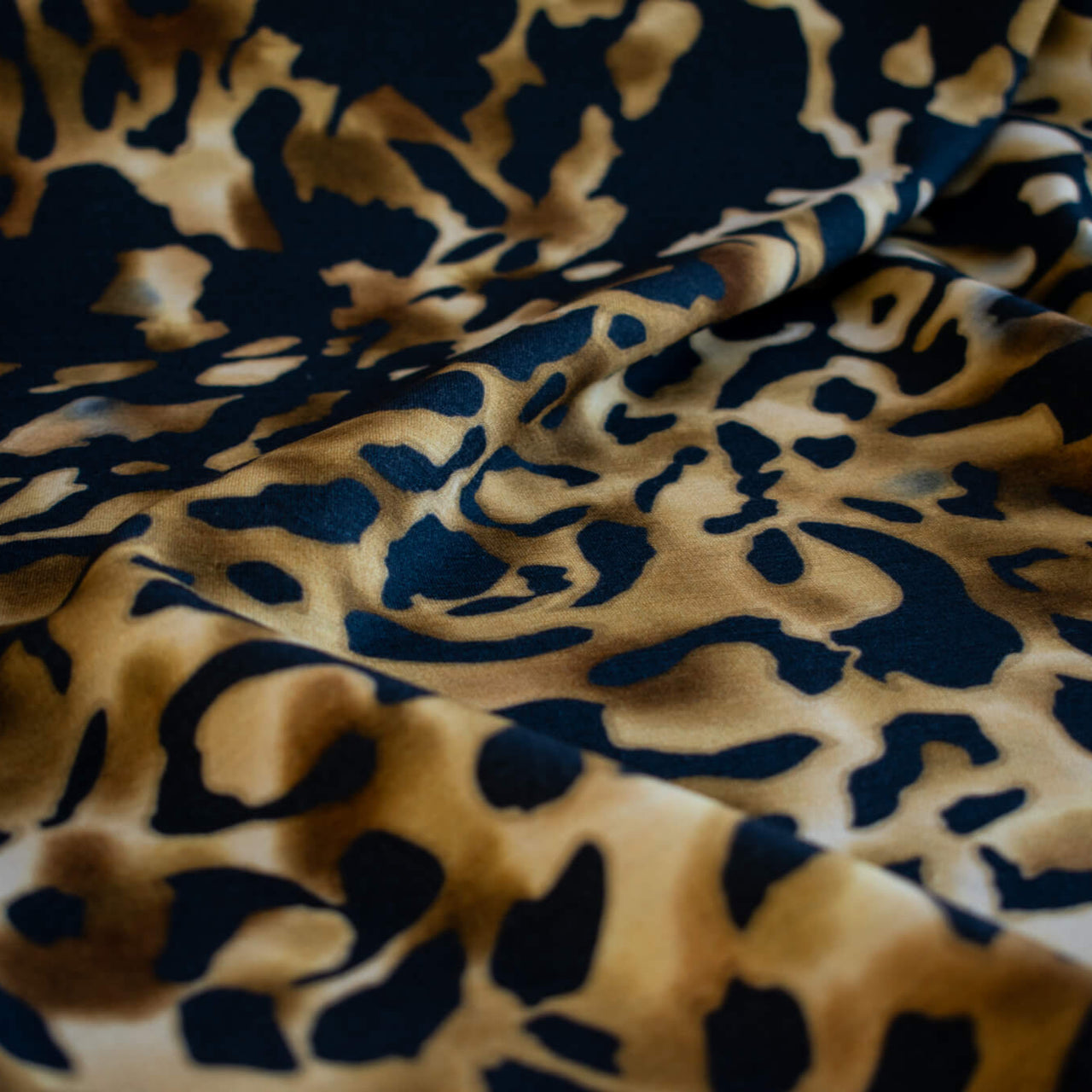 Italian Animal Print Wool Blend Jersey knit fabric by the yard. Shades of gold and cream flow against dramatic coal a bits of blue to create a vibrant and sophisticated animal print design. This would make a lovely wrap style long cardigan, a bold fitted sheath dress, or pencil skirt. Close up image.