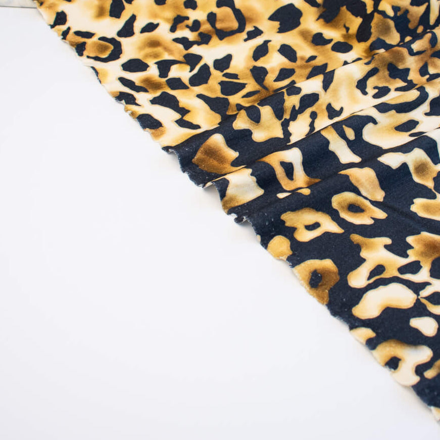 Italian Animal Print Wool Blend Jersey knit fabric by the yard. Shades of gold and cream flow against dramatic coal a bits of blue to create a vibrant and sophisticated animal print design. This would make a lovely wrap style long cardigan, a bold fitted sheath dress, or pencil skirt. Image of selvedge.