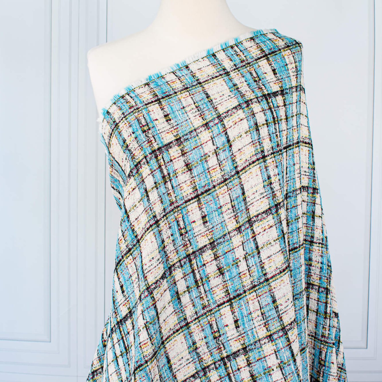 Couture Designer Italian Cotton Blend Ch@nel Boucle fabric by the yard in a gorgeous light tropical blue, black and ivory plaid accented by yellow and red fibers. This soft boucle has a textured hand and beautiful drape. Image of fabric draped on dressform.