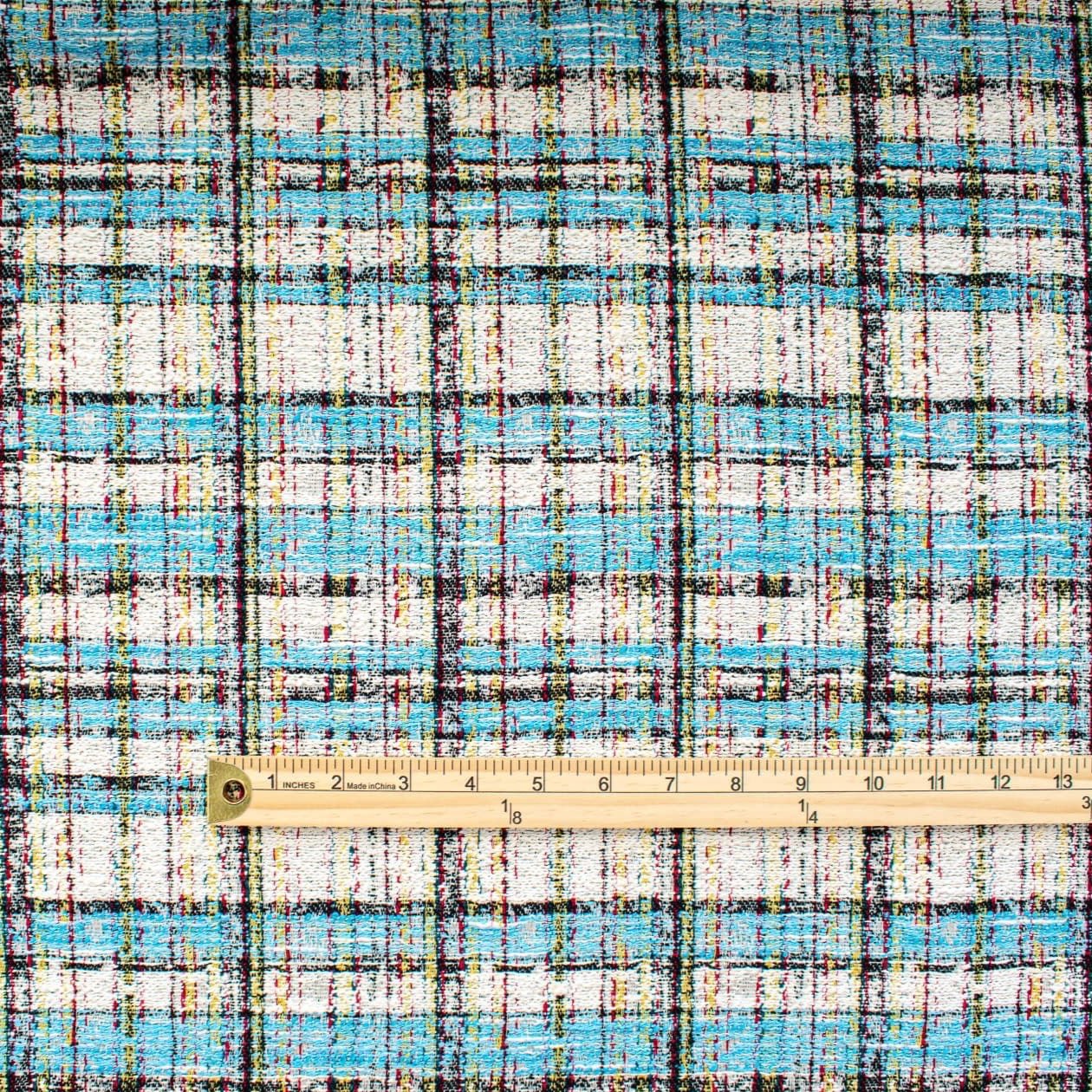 Couture Designer Italian Cotton Blend Ch@nel Boucle fabric by the yard in a gorgeous light tropical blue, black and ivory plaid accented by yellow and red fibers. This soft boucle has a textured hand and beautiful drape. Image of pattern scale with ruler.