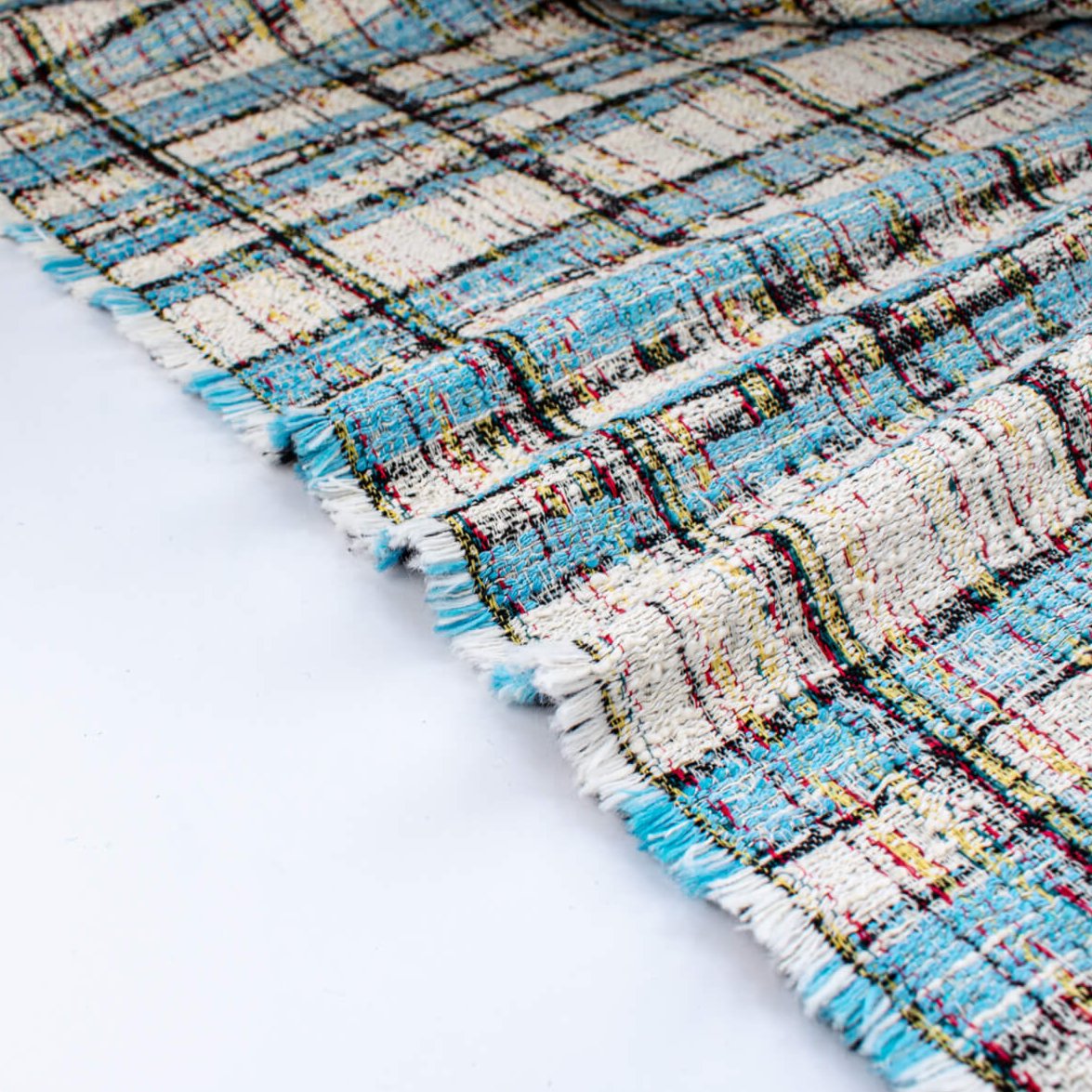 Couture Designer Italian Cotton Blend Ch@nel Boucle fabric by the yard in a gorgeous light tropical blue, black and ivory plaid accented by yellow and red fibers. This soft boucle has a textured hand and beautiful drape. Image of selvedge.