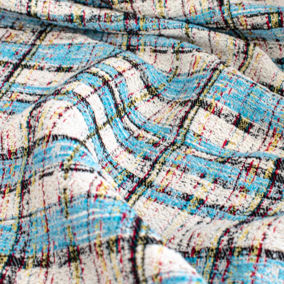 Couture Designer Italian Cotton Blend Ch@nel Boucle fabric by the yard in a gorgeous light tropical blue, black and ivory plaid accented by yellow and red fibers. This soft boucle has a textured hand and beautiful drape. Close up image.