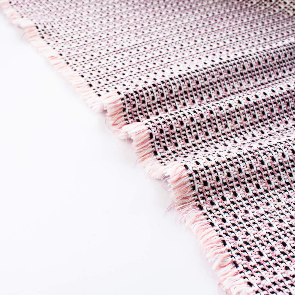 Our Couture Cotton Blend Designer Tweed fabric by the yard will have you 'Blushing' with excitement! Just in from Italy, this Ch@nel tweed is just lovely with its soft hand and elegant drape and features shades of pink, white, black, and red. Image of selvedge.