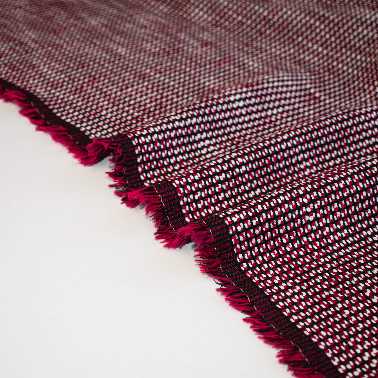 Close-up of selvedge of a Couture textured woven fabric with red and black pattern on a white background