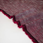 Close-up of selvedge of a Couture textured woven fabric with red and black pattern on a white background