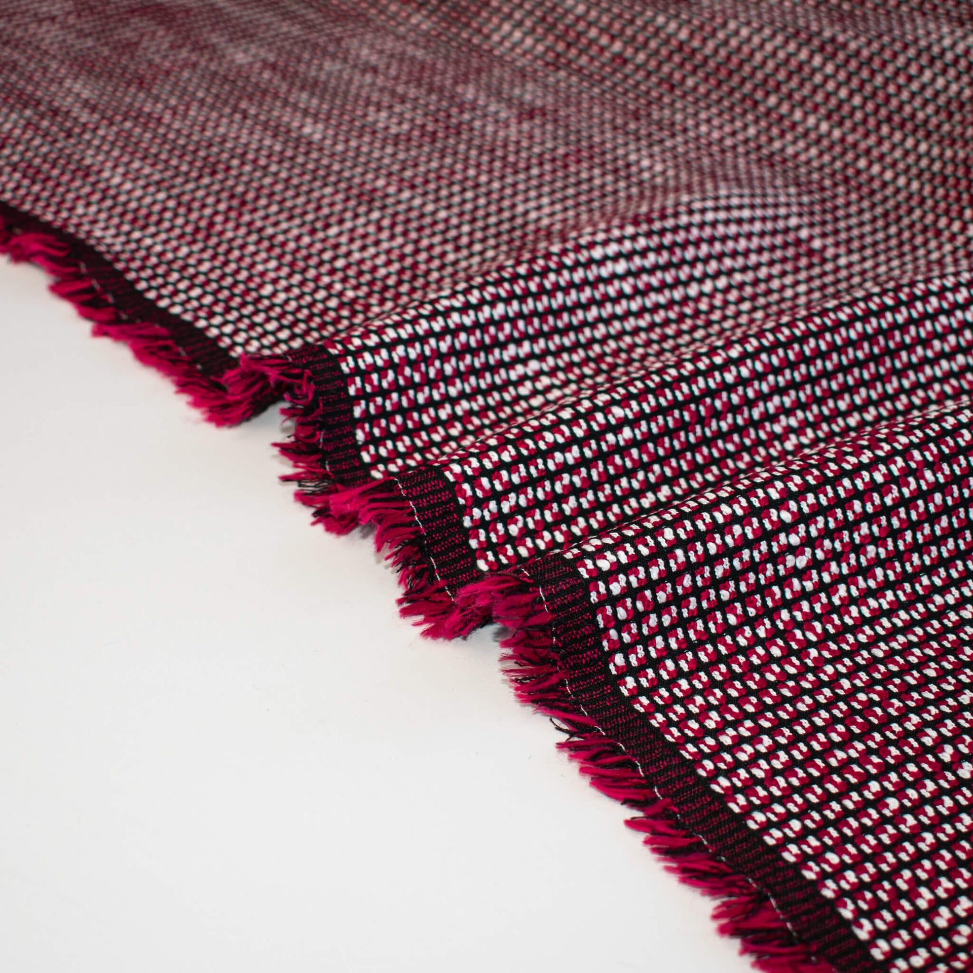 Close-up of selvedge of a Couture textured woven fabric with red and black pattern on a white background