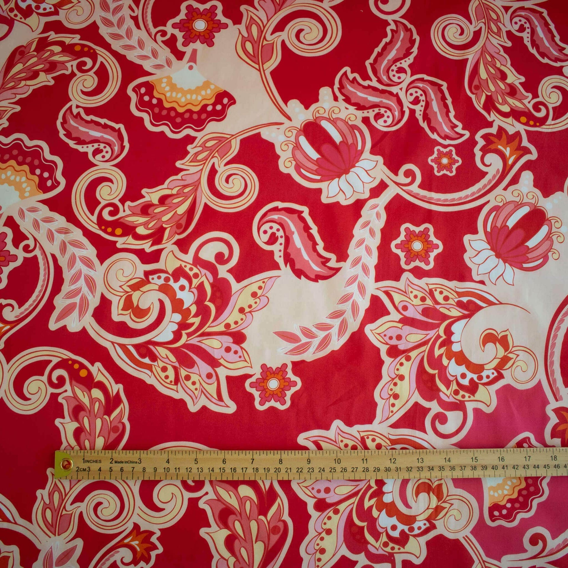 A close-up of Italian Viscose Coral Red Paisley woven fabric, with a wooden ruler at the bottom for scale.