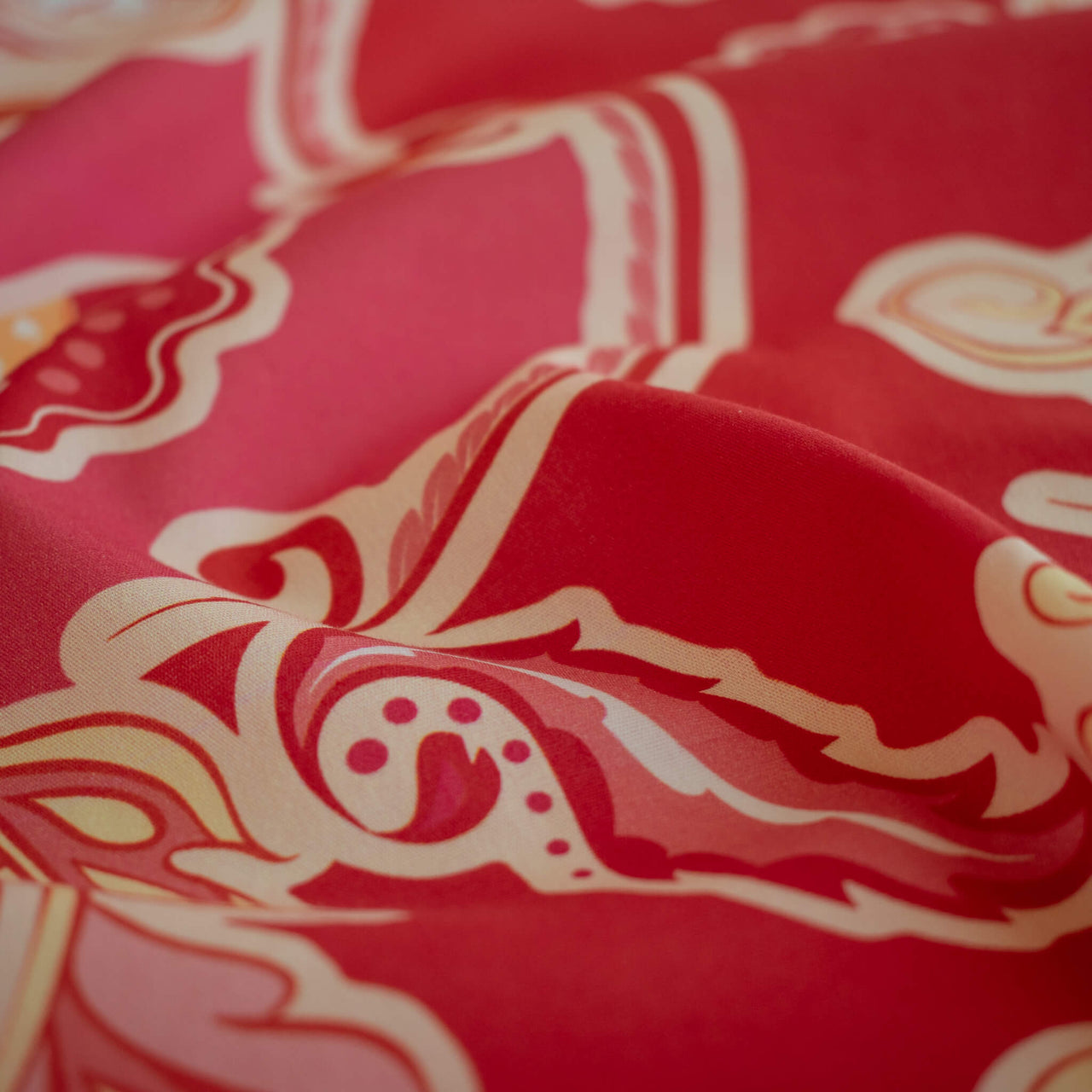 A close-up of Italian Viscose Coral Red Paisley woven fabric by the yard. A fresh and vibrant natural fiber that has the drape of a shirt weight and falls away from the body.
