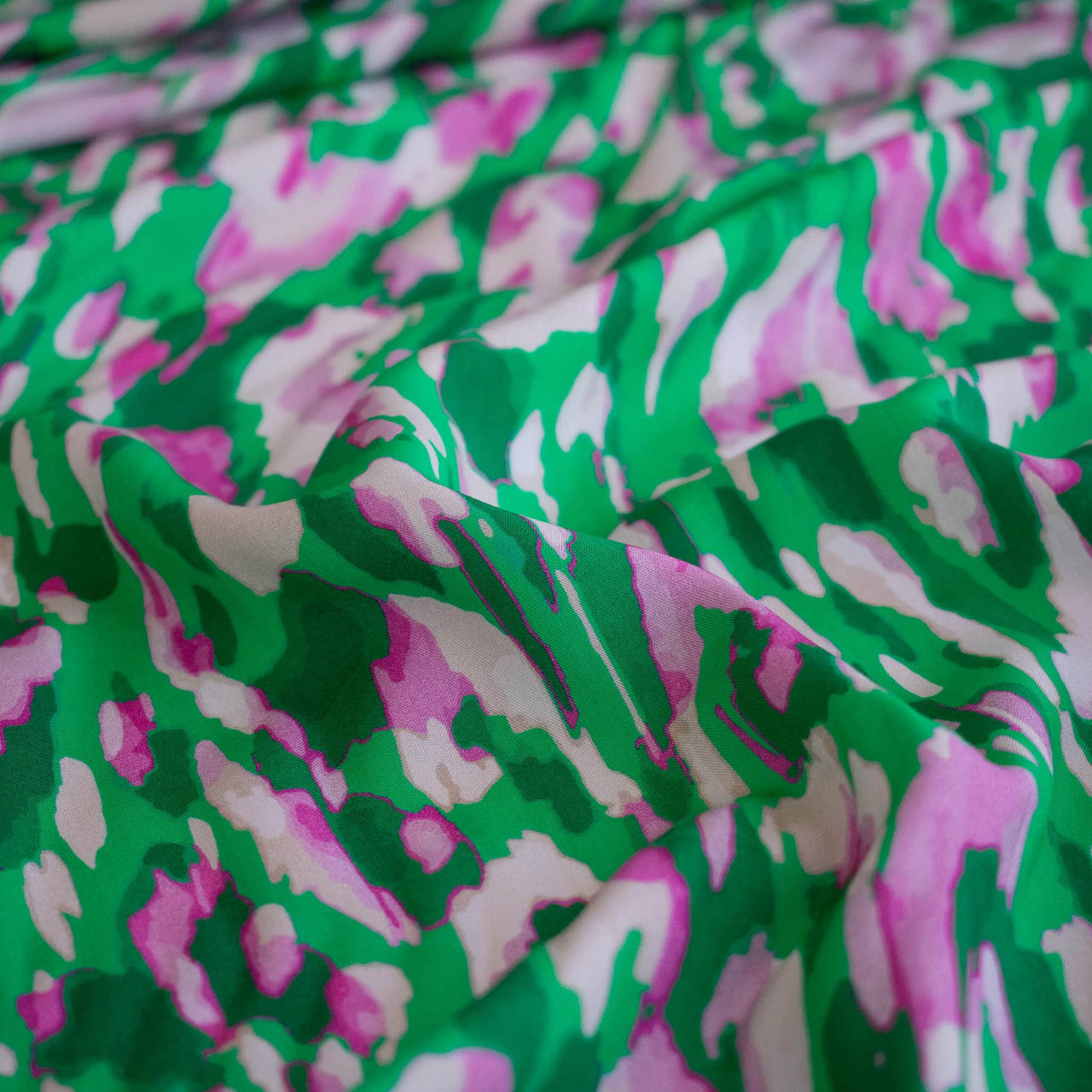 Close up image of Italian Viscose Woven Abstract Print fabric by the yard in a fresh emerald green and soft pink abstract print. 