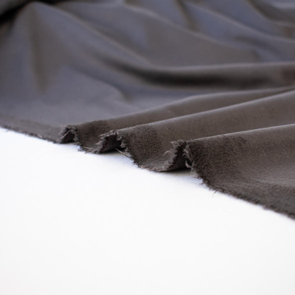 Faux Suede Knit fabric by the yard in a neutral truffle brown color . It has a soft hand, elegant drape and tons of edgy sophistication! Faux suède has a soft napped surface which requires cutting your fabric out in a one-way nap direction. Image of fabric  selvedge.