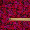 Italian woven viscose crepe fabric by the yard. Beautiful blooms are perfect when you want to add a burst vibrant color! Richly printed in shades of red, pink and lilac with vibrant green leaves set against a black background.  Image of fabric pattern scale with ruler.