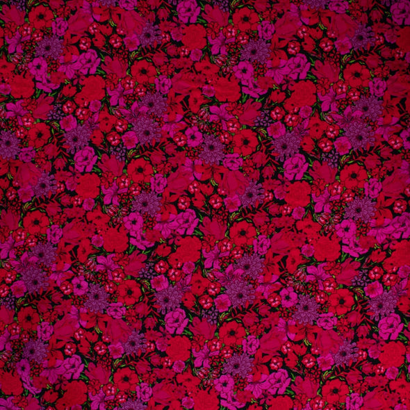 Italian woven viscose crepe fabric by the yard. Beautiful blooms are perfect when you want to add a burst vibrant color! Richly printed in shades of red, pink and lilac with vibrant green leaves set against a black background.  Image of fabric pattern.