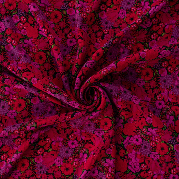 Italian woven viscose crepe fabric by the yard. Beautiful blooms are perfect when you want to add a burst vibrant color! Richly printed in shades of red, pink and lilac with vibrant green leaves set against a black background.  Image of fabric body.