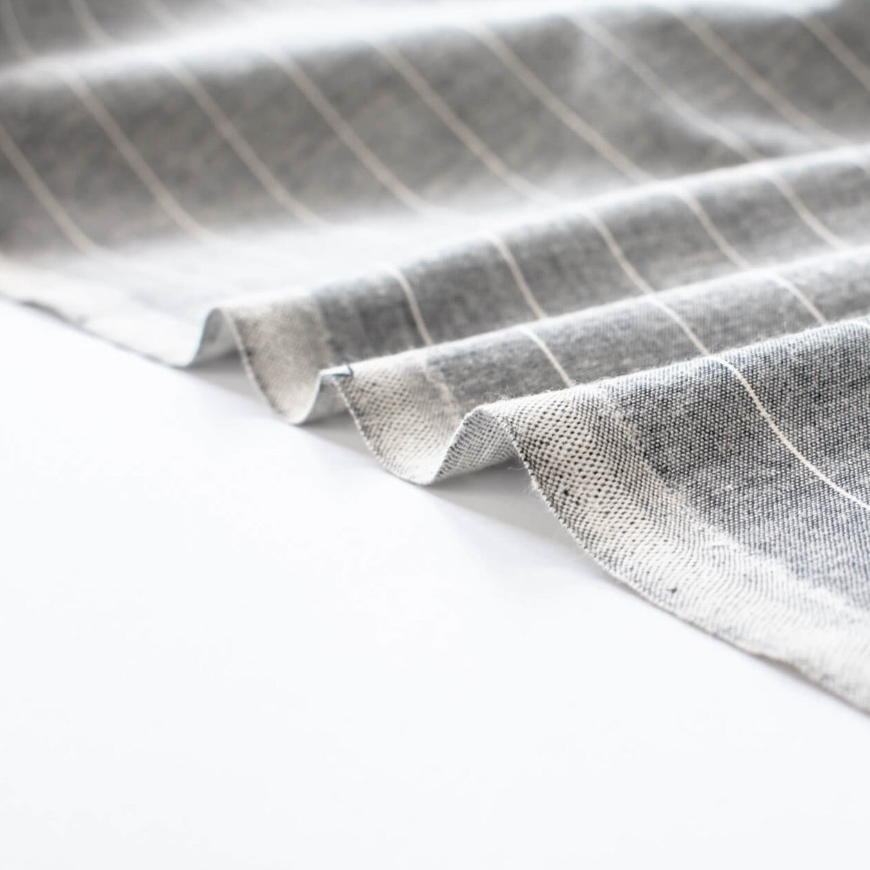 Cotton/Linen Chambray fabric by the yard. On the lighter side of mid-weight, this woven dark navy chambray features a white vertical pinstripe, a nice comfortable hand, and a lovely drape. Image of fabric selvedge