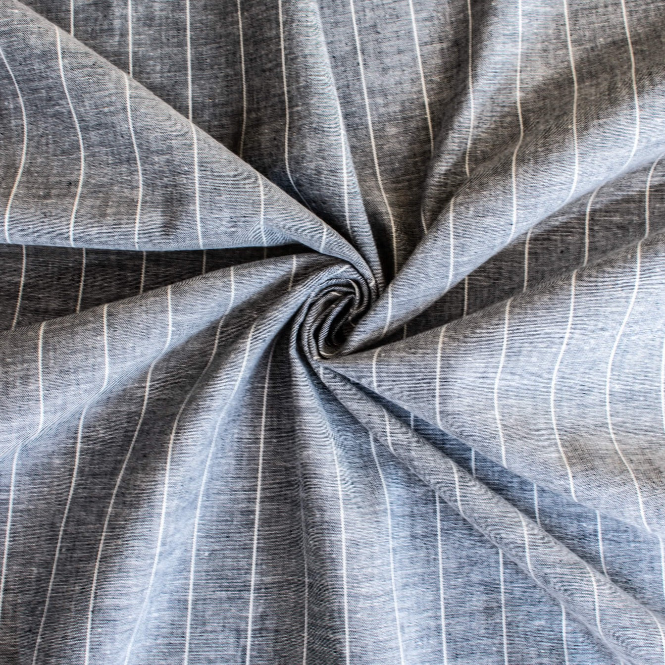 Cotton/Linen Chambray fabric by the yard. On the lighter side of mid-weight, this woven dark navy chambray features a white vertical pinstripe, a nice comfortable hand, and a lovely drape.  Image of fabric body.