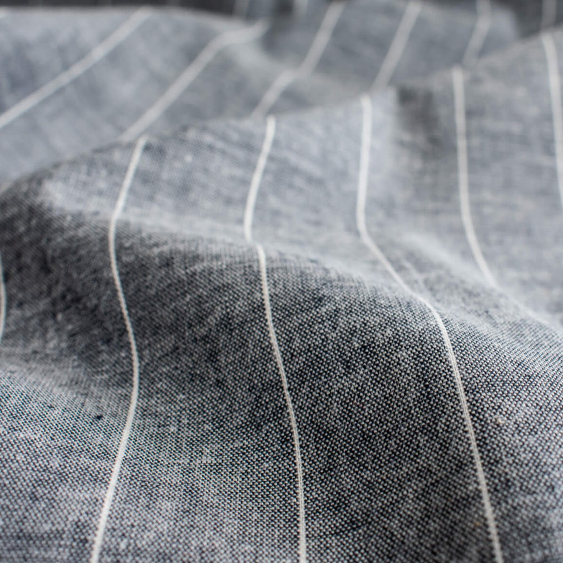 Cotton/Linen Chambray fabric by the yard. On the lighter side of mid-weight, this woven dark navy chambray features a white vertical pinstripe, a nice comfortable hand, and a lovely drape.  Close up image.