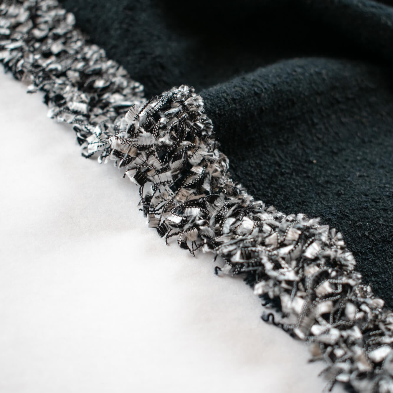 Exquisite Mokuba passementerie trim in black and silver chenille ribbons perfect for your next couture classic French jacket. Close up of trim displayed upon black boucle fabric.